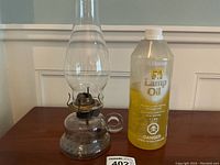 Photo of antique clear glass oil lamp with metal burner and chimney next to a 1 liter bottle of yellow lamp oil.