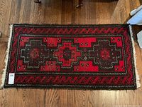 Full view of the upright rectangular carpet showing the overall geometric design, colors, and dimensions relative to wooden floor. Shows condition and fringed edges.