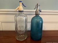 Full view of both soda siphons showing clear etched logo and blue glass one with metal top.