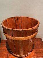 Front view of the antique wooden bucket showing vertical slats and two horizontal bands.