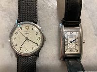 Both watches side by side; round Timex with scratched white dial and textured black strap, rectangular Coach with patterned dial and black leather strap