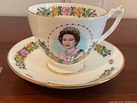 Side view of the limited edition Coalport cup featuring Queen Elizabeth portrait and floral garland on the front, with gold rim and handle details.