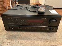 Front angle view of Denon AVR-1805 AV receiver with remote control on top, showing buttons, dials and power switch.