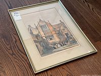 Framed English Romantic print showing a Tudor-style house with three people sitting on a stone bench in the garden in front of it.