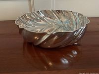 Side angle view showing scalloped edge and leaf vein texture inside the silver plate bowl.