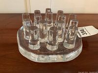 Clear glass tea pot holder trivet with multiple cylindrical vertical glass pegs, viewed at an angle showing shape and height of pegs.