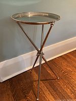 Side view of stainless steel tripod side table showing the slender legs and round tray top with raised edge.