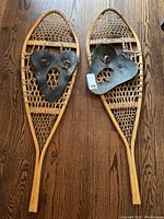 Full view of both wooden snowshoes showing the woven rawhide and black rubber bindings on wood frames.