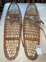 Pair of vintage wooden frame snowshoes with rawhide webbing and leather bindings displayed on a table, showing full length.