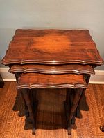 Photo of three walnut nesting tables stacked together showing scalloped tops and turned legs.