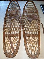 Full view of the pair of wooden frame snowshoes side by side showing rawhide lacing and leather bindings