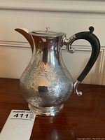 Front-facing view of sterling silver hot water pot showing full incised pattern and ebony handle