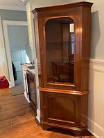 View of solid walnut corner cabinet showing glass display door and lower cabinet door, wood grain visible, in a room corner.