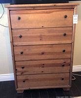 Front view of a 5-drawer wood dresser with natural finish and black square drawer knobs.