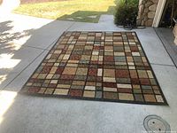 Full view of rug laid out showing overall geometric square pattern and colors under daylight.
