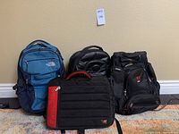 Overview of the three backpacks: North Face blue backpack, black elleven backpack with Adobe logo, black SwissGear computer messenger bag with red