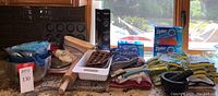 Wide view of all items displayed on kitchen counter including bread baskets, rolling pin, baking pans, Ziploc bags, oven mitts, dish towels, and mortar and pestle.