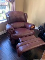 View of the brown faux leather recliner chair with the footrest extended, showing padded armrests and backrest with nailhead trim
