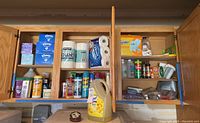 Wide shot of household cleaning supplies and paper products neatly arranged inside wooden cabinets