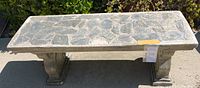 Top-down view of the rectangular stone inlaid bench seat showing the pattern of various stone segments embedded in the concrete