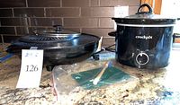 Photo shows Japanese electric grill with power cord, Crock-Pot slow cooker, cleaning brush and green cleaning pad on countertop.