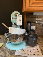 Front view of mixer with bowl, splash guard, instruction sheet and nearby accessories
