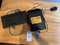 Top view of projector body with wired keyboard, IR remote and power adapter on wooden surface