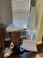 Overall view of lot showing ironing board, wicker laundry basket, Panasonic steam iron, Fitbit scale, drying rack, pillow packaging, and heating pad.