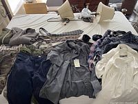 Photo showing a variety of men's shirts in different shades, 3 neck ties, and 2 canvas belts on a table alongside a light-colored hoodie and jacket.
