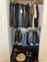 Full view of the closet showing jackets, pants, shirts on hangers, belts on floor, and hats on floor under clothes.