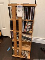 Wooden rotating CD stand holding multiple shelves of CDs, standing next to a white door and on wooden floor.