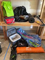 Wide view of most items on wood shelves showing bags, blankets, cooler bags, mats, inflatable water float, and tent bag.