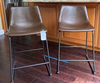 Two brown faux leather bar stools with black metal frames placed side by side, showing overall shape and design.