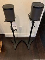 Two Sonos Play:1 speakers mounted on black adjustable stands against a wall.