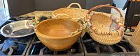 Photo showing silver plate trays, wood salad bowl with brass deer-head handles, and two woven baskets on a stove surface.