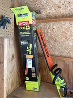 Ryobi 22" cordless hedge trimmer in box with visible branding and key features like rotating handle, 3/4" cut capacity, and HedgeSweep debris remover attachment