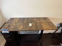 Full view of the standing desk with rustic brown wood grain top and control panel on left side among black legs.