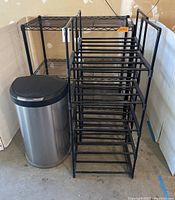 Photo showing 3-tier black metal rack, two black plastic racks with 5 shelves each, and Simple Human trash can with motion sensor lid