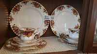Two complete 5-piece place settings showing different angles and arrangement of plates and cups with floral pattern and gold trim