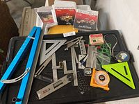 Overview of assorted angle measuring tools and manuals on a black tray including large blue angle locator, plastic angle guides, metal protractors, and others.