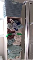 Photo showing a collection of rolled and folded bath towels and hand towels in various colors stacked in a white shelving unit.