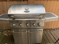 Full front view of large stainless steel BBQ grill with five burner controls and temperature gauge on lid.