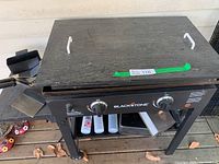 Blackstone propane grill with closed cooking surface and side handles visible, including spatula and scraper on side tray.