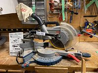 Front view of Bosch slide miter saw on workbench with dust bag and instruction manual