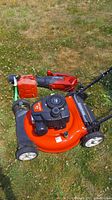 Red Craftsman M105 lawn mower on grass with engine and cutting deck visible, alongside a red and black gas jug.