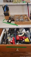 Full view of counter top showing wooden knife block with knives, bamboo cutlery tray with organized flatware, and drawer open with assorted kitchen tools and gadgets.