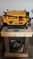 Full view of planer mounted on wooden cabinet with coiled dust hose underneath