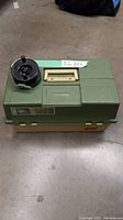 Closed view of vintage green fishing tackle box with attached fishing reel on exterior.