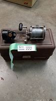 Vintage open face fishing reel mounted on a brown plastic tackle box.