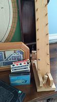 Wooden crib board with pegs and carved indigenous artwork next to wooden toy playing cards in frame and other wooden game parts.